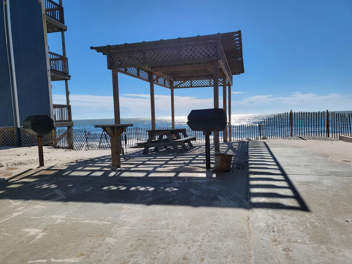 An inviting exterior space featuring a wooden gazebo, picnic table, and grill stations with an ocean view. The communal setup encourages socializing, outdoor meals, and enjoying the sea breeze, tying into the idea of spontaneous family feasts and shared adventures.