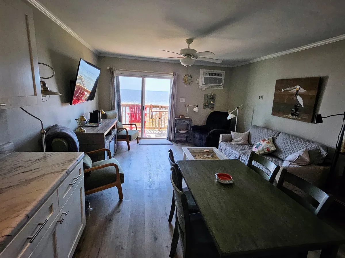This image captures the dining table situated near a large window that offers spectacular ocean views. Comfortable seating and a relaxed living space are visible, suggesting lingering meals and time spent enjoying scenery and each other’s company.
