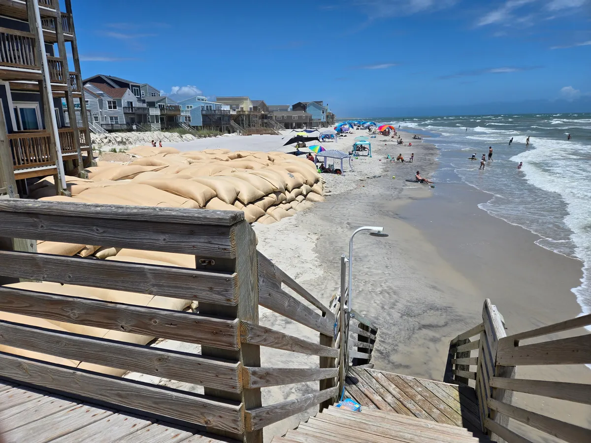 A vibrant exterior scene of beachfront homes, with people enjoying the sandy shores under umbrellas, children playing in the sand, and gentle waves in the background. The image conveys a vacation-like, lively atmosphere ideal for families and groups making the most of their seaside escape.