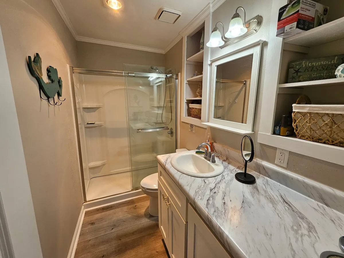 A fresh, spa-inspired bathroom featuring a modern shower area, vanity with sink, spacious mirror, and organized storage shelves. The atmosphere is tranquil and clean, inviting guests to unwind and refresh.